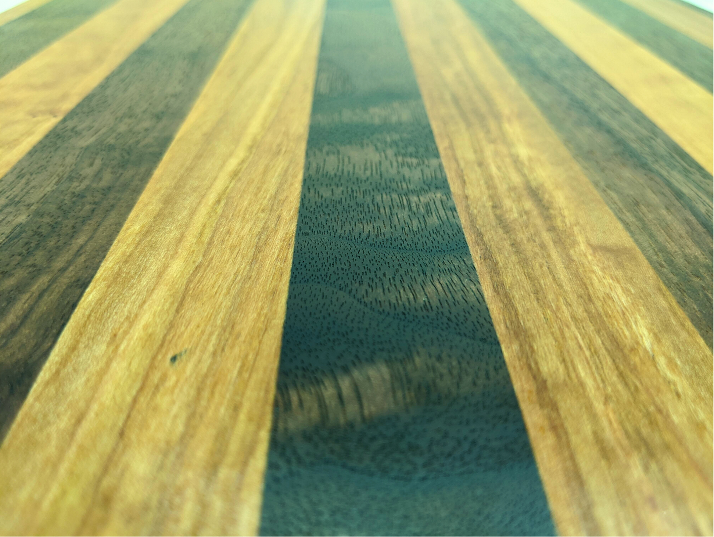 A close‑up of a handcrafted Walnut and Cherry cutting board showing its alternating hardwood stripes, smooth edge‑grain construction, and polished food‑safe finish. The warm Cherry tones contrast with the deep brown Walnut, highlighting the board’s premium craftsmanship and durable, handmade quality — ideal for shoppers searching for a Walnut and Cherry cutting board, artisan kitchen gift, or chef‑quality prep board.