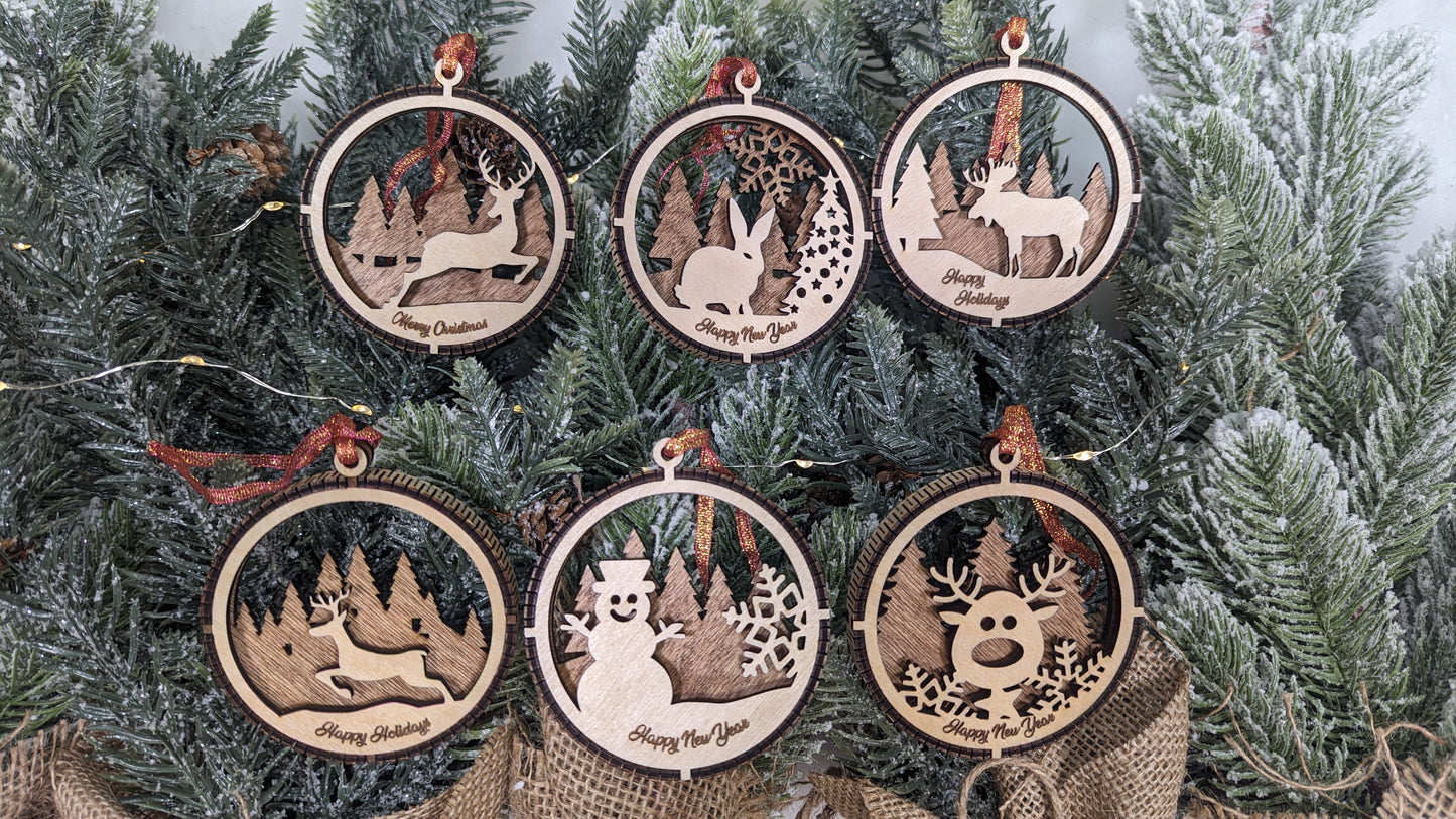 Close-up of six laser-cut wood ornaments on pine branches. Designs include a rabbit in the woods, a moose with "Happy Holidays," a reindeer with "Merry Christmas," and a snowman with "Happy New Year." Each 3D layered ornament features the signature living hinge flexible wood wrap and copper ribbon. Handcrafted by Great Scott Woodworks, these rustic birch or basswood decorations are perfect for woodland-themed holiday decor or a high-quality gift set.