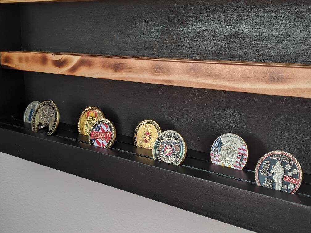 A wider view of a handcrafted wooden challenge coin display featuring dark‑stained wood with a lightly burnt pecan‑stained accent along the top shelf. Multiple Marine Corps–themed challenge coins, including Semper Fi and veteran designs, rest securely in the slotted grooves. This image highlights the display’s capacity, craftsmanship, and suitability for military collectors, patriotic décor, and veteran gifts.
