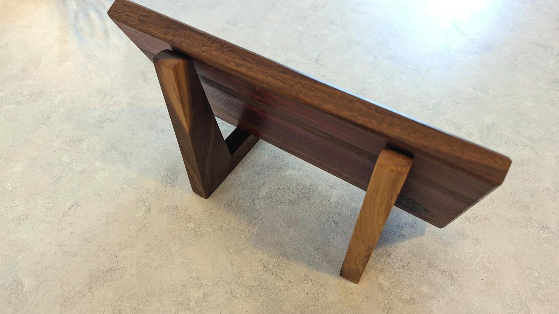 High-angle view of a dark walnut cutting board resting in a pair of matching walnut L-shaped stands. This perspective highlights the low-profile 90-degree design that provides maximum stability while keeping the board's surface fully visible. Handcrafted by Great Scott Woodworks, these solid hardwood holders are perfect for displaying artisanal boards on a kitchen counter or providing a secure, upright position for air-drying.