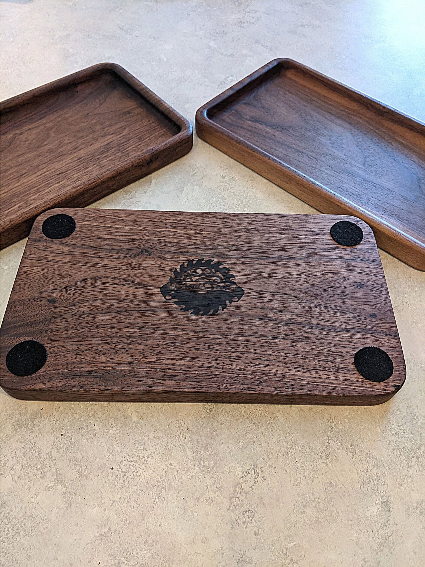 Three walnut catch-all trays displayed together, one turned over to show felt pads and Great Scott Woodworks logo etched on the bottom