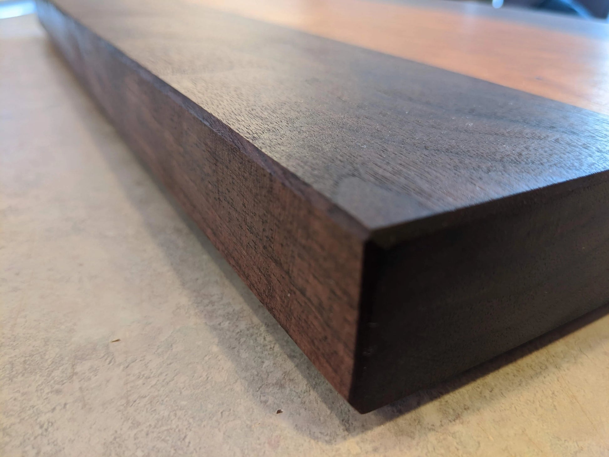 A close‑up of a handcrafted Walnut cutting board with rich dark grain and a smooth, polished food‑safe finish, resting on a light countertop. The clean edges and deep brown hardwood tones highlight the premium craftsmanship — ideal for shoppers searching for a Walnut cutting board, handmade kitchen gift, or artisan charcuterie board.